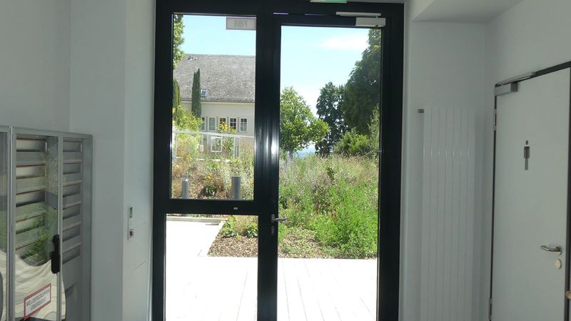 Eine große Glastür in einem Gebäude, die einen Ausblick auf einen grünen Garten bietet.