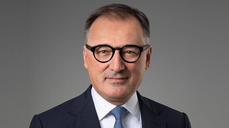 Ein Porträt eines Mannes mit Brille in einem Anzug vor grauem Hintergrund.