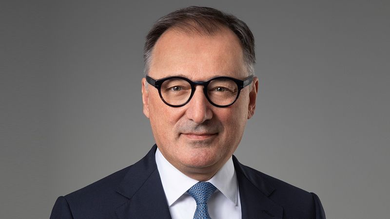 Ein Porträt eines Mannes mit Brille in einem Anzug vor grauem Hintergrund.