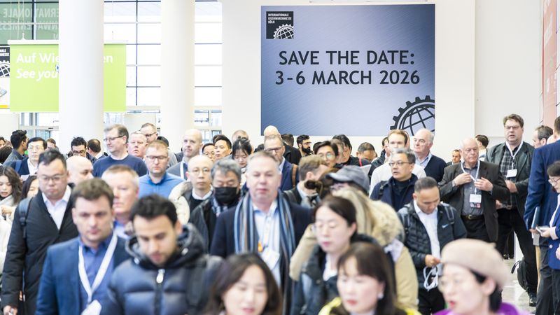 Eine große Gruppe von Messebesuchern geht durch eine Messehalle, im Hintergrund ist ein "Save the Date" Schild für März 2026 zu sehen.