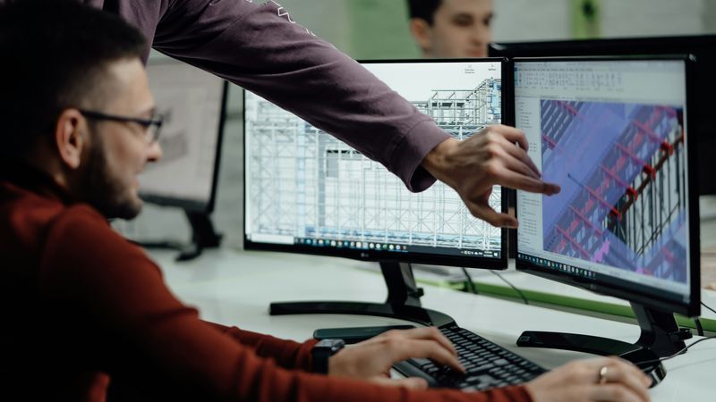 Zwei Personen arbeiten gemeinsam an einem Computer, wobei eine Person auf den Bildschirm zeigt.