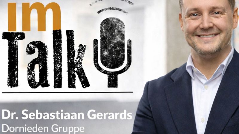 Ein Mann im Anzug steht neben einem großen Mikrofon-Logo mit der Aufschrift "im Talk".
