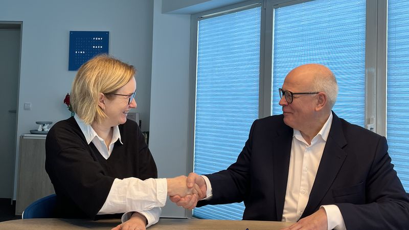 Zwei Personen geben sich die Hand bei einer Vertragsunterzeichnung in einem modernen Büro.