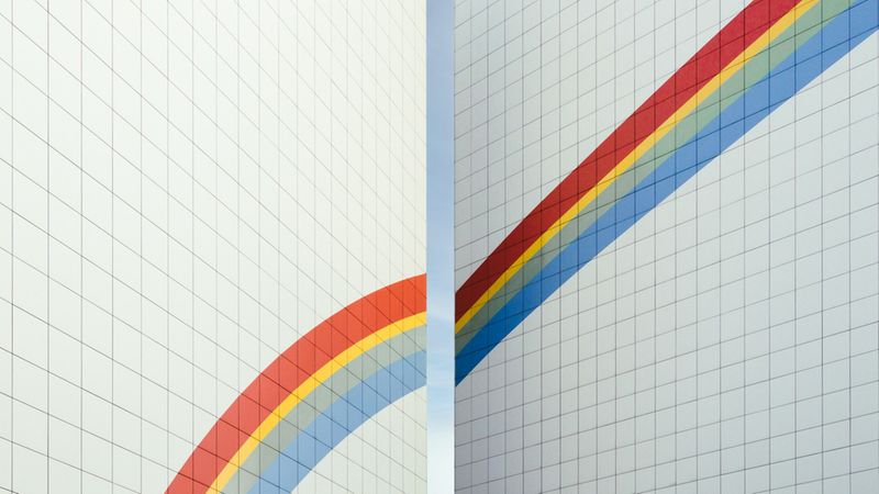 Zwei parallel stehende Hochhausfassaden mit einem aufgemalten Regenbogen