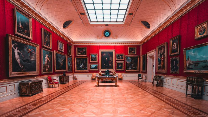 Ein prächtiger Innenraum einer Kunstgalerie mit roten Wänden, verziert mit zahlreichen Gemälden und einem kunstvollen Holzboden.