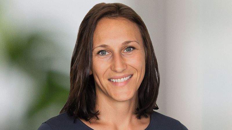 Ein Porträt einer lächelnden Frau vor einem unscharfen Hintergrund.