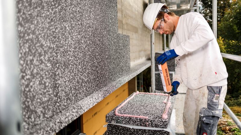 Ein Handwerker installiert Wärmedämmung an einem Gebäude.