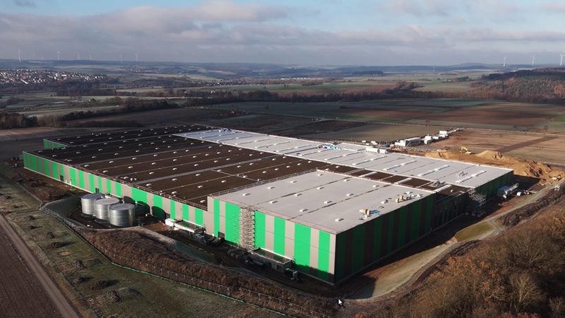 Luftaufnahme eines großen Logistikzentrums in ländlicher Umgebung mit grünen und braunen Fassaden.