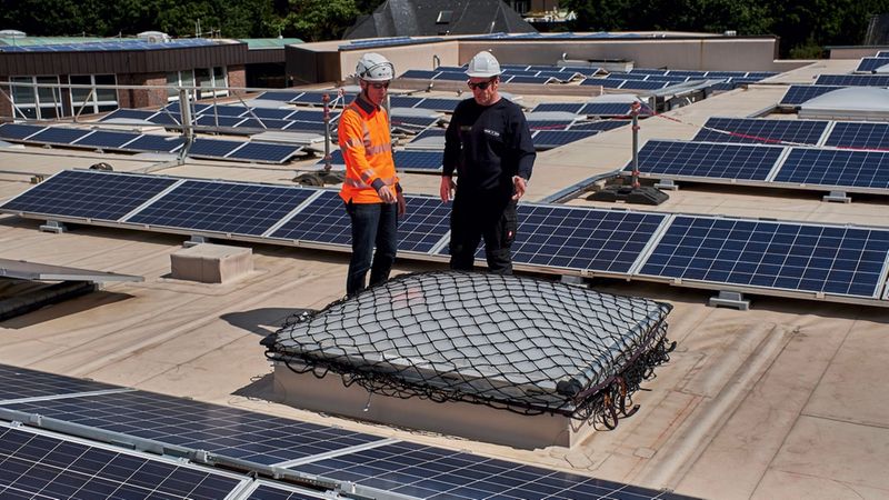 Zwei Arbeiter inspizieren eine Lichtkuppel auf einem Flachdach.