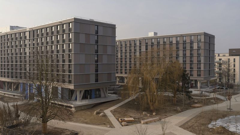 Ein modernes Wohngebäude mit mehreren Etagen und einer minimalistischen Architektur, umgeben von einem neu angelegten Park.