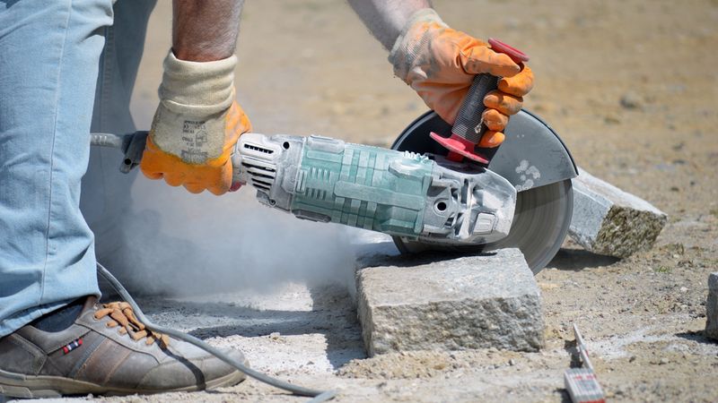 Ein Arbeiter schneidet mit einem Trennschleifer einen Steinblock auf einer Baustelle.