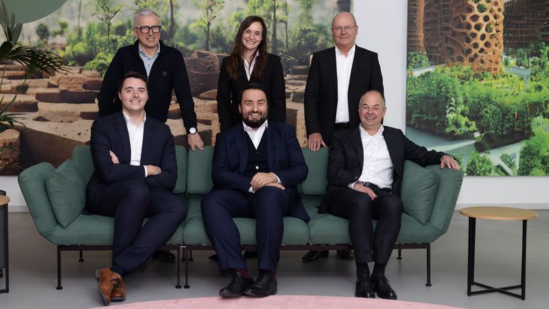 Eine Gruppe von sechs Personen posiert vor einem großen Bild mit Pflanzenmotiven.