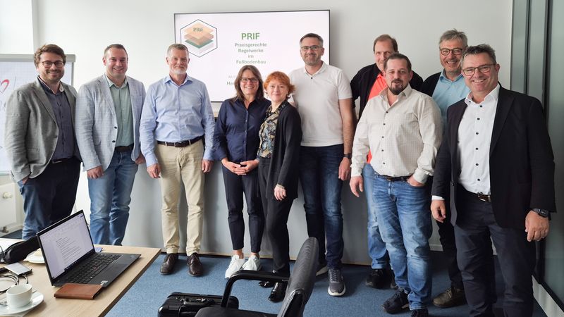 Eine Gruppe von Menschen steht vor einer Präsentation in einem Konferenzraum.