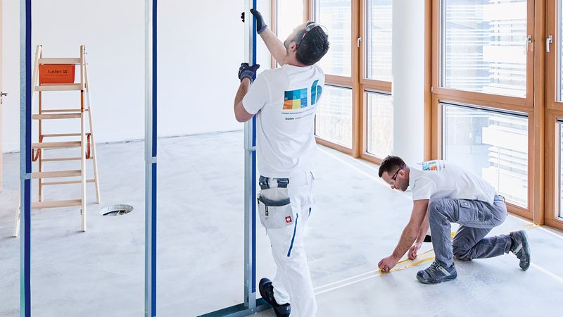 Zwei Monteure beim Innenausbau, die eine Metallrahmenkonstruktion in einem hellen Raum installieren.