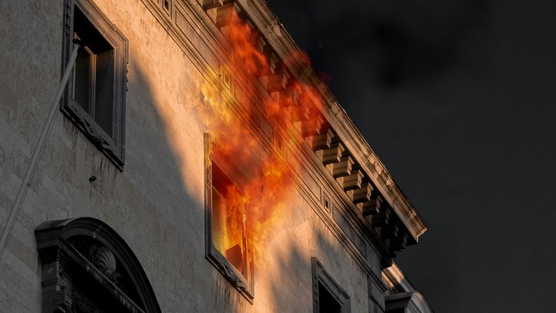 Ein Feuer bricht aus einem Fenster eines historischen Gebäudes in der Nacht aus.