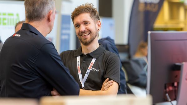 Zwei Männer unterhalten sich bei einem Geschäftstreffen. Einer der Männer trägt ein Namensschild mit der Aufschrift "EASTWOOD".