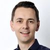 Ein Porträt einer lächelnden Person in einem dunkelblauen Hemd vor einem weißen Hintergrund.
