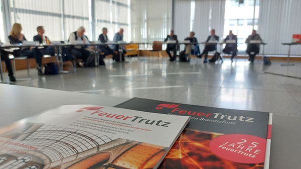 Zwei Ausgaben des FeuerTrutz Magazins liegen auf einem Tisch, im Hintergrund Personen aus dem Redaktionsbeirat