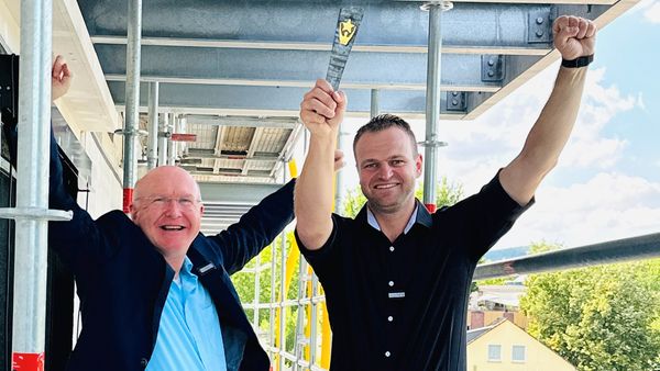 Zwei Männer feiern ein Richtfest auf einem Baugerüst.