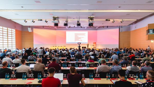 Ein großer Konferenzraum voller Teilnehmer, die einer Präsentation folgen.