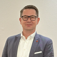 Ein Mann mit Brille in einem Anzug vor einem neutralen Hintergrund.