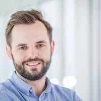 Ein Porträt eines lächelnden Mannes in einem hellen Raum.