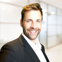 Ein Mann in einem Anzug lächelt in die Kamera, während er in einem modernen Büro steht.