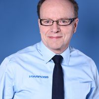 Ein Mann mit Brille und blauem Hemd steht vor einem blauen Hintergrund.