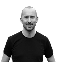 Ein Porträt eines lächelnden Mannes in einem schwarzen T-Shirt vor weißem Hintergrund.