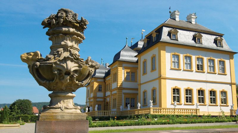 Ein prächtiges Barockschloss mit einer kunstvollen Steinskulptur im Vordergrund.
