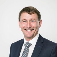 Ein lächelnder Mann in einem Anzug vor einem neutralen Hintergrund.