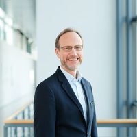 Ein lächelnder Mann im Anzug steht in einer modernen Büroumgebung.