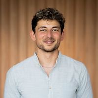 Ein Porträt eines lächelnden Mannes in einem hellen Hemd vor einem neutralen Hintergrund.