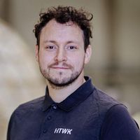 Ein Mann in einem schwarzen Poloshirt mit dem Aufdruck "HTWK" steht vor einem unscharfen Hintergrund.