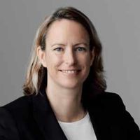 Porträt einer lächelnden Frau in einem schwarzen Blazer vor grauem Hintergrund.