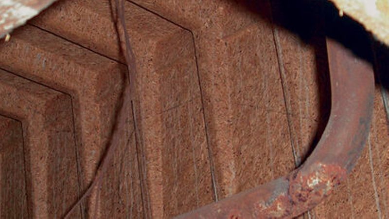 Ein rostiges Rohr in einem alten Gebäude mit bröckelnden Wänden und sichtbaren Holzbalken.