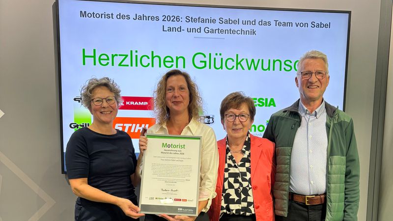 Vier Personen stehen lächelnd auf einer Bühne vor einem Bildschirm mit der Aufschrift 'Motorist des Jahres 2026' und halten eine offizielle Auszeichnungsurkunde für Stefanie Sabel und das Team von Sabel Land- und Gartentechnik in die Kamera.