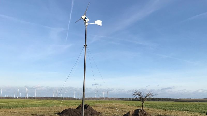 Eine kleine Windkraftanlage steht auf einem weiten Feld unter blauem Himmel.