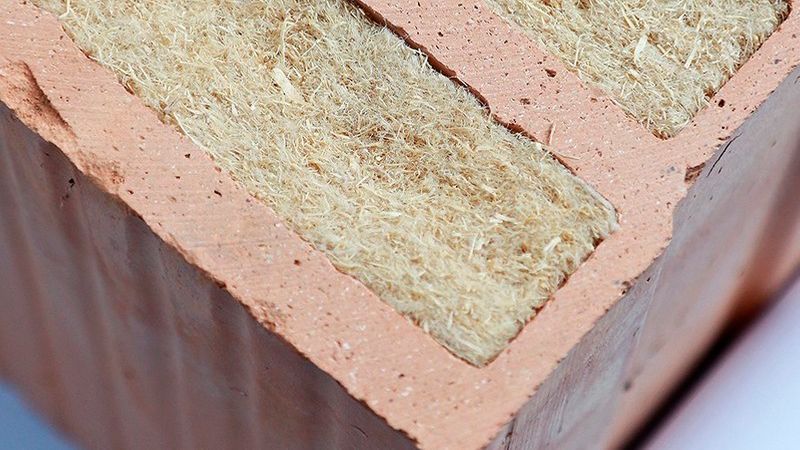 Nahaufnahme eines modernen Ziegelsteins, der mit natürlichem Dämmstoff, wahrscheinlich Holzwolle oder Holzfasern, gefüllt ist, um die Wärmedämmung im Mauerwerk zu optimieren.