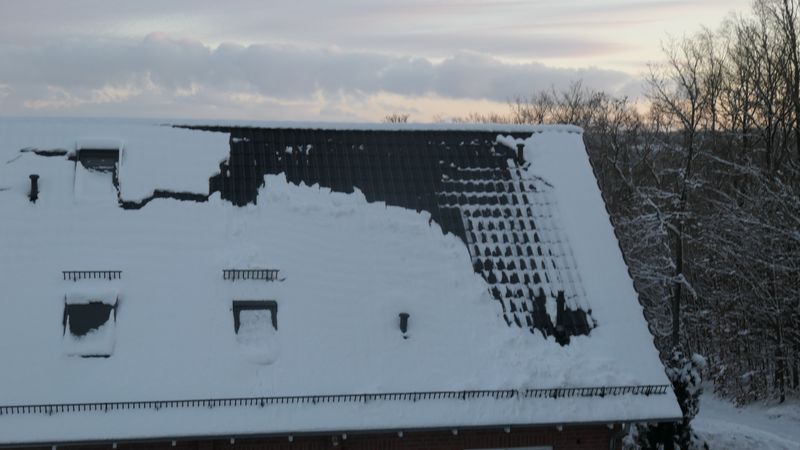 Schneebedecktes Einfamilienhausdach mit teilweise rutschendem Schnee