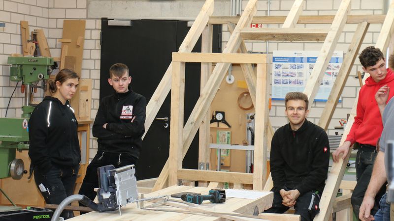 Eine Gruppe von Auszubildenden in einer Werkstatt, die an einem Holzprojekt arbeiten.