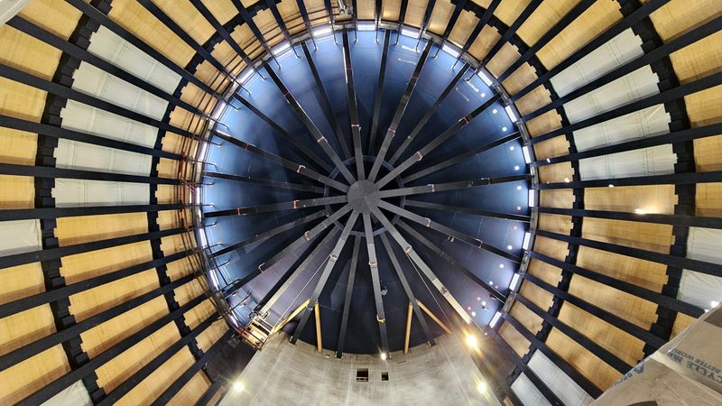 Innenansicht einer großen Kuppel mit sichtbaren Stahlträgern und Holzverkleidung.