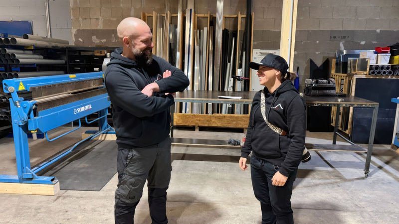 Zwei Personen unterhalten sich in einer Werkstatt neben einer blauen Metallmaschine.