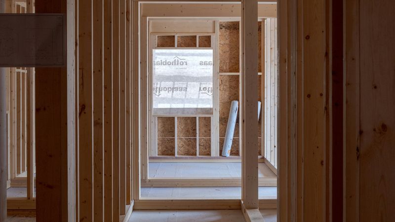 Innenansicht eines im Bau befindlichen Holzrahmenbaus mit sichtbaren Holzbalken und unvollendeten Wänden.