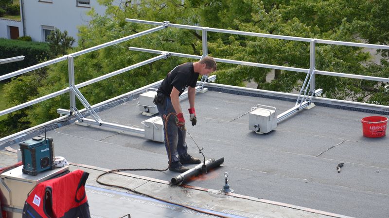 Ein Handwerker bei der Abdichtung eines Flachdachs mit Bitumenbahnen.