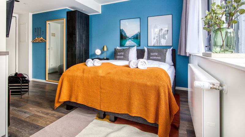 Ein modernes Schlafzimmer mit einem großen Bett, blauer Akzentwand und stilvollen Dekorationen.