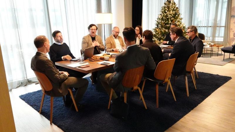 Ein Team von Geschäftsleuten sitzt in einem Konferenzraum um einen Tisch, während im Hintergrund ein geschmückter Weihnachtsbaum steht.