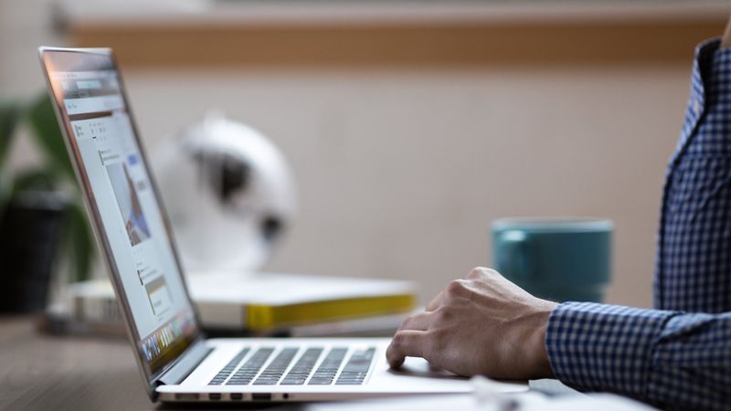 Eine Person arbeitet an einem Laptop, während ein Notizbuch auf dem Tisch liegt.