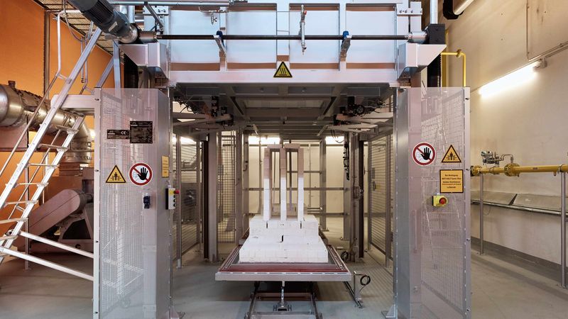 Ein moderner industrieller Ofen in einer Fabrikumgebung, umgeben von Metallstrukturen und Sicherheitswarnungen.