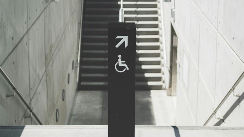 Ein moderner, barrierefreier Zugang mit einer Treppe und einem Hinweisschild für Rollstuhlfahrer.